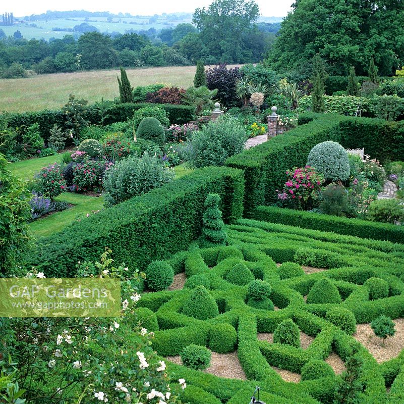 View of Knot and Silver Pear gardens separated from herbaceous borders by yew hedge. Rural landscape of fields, woods and hills.