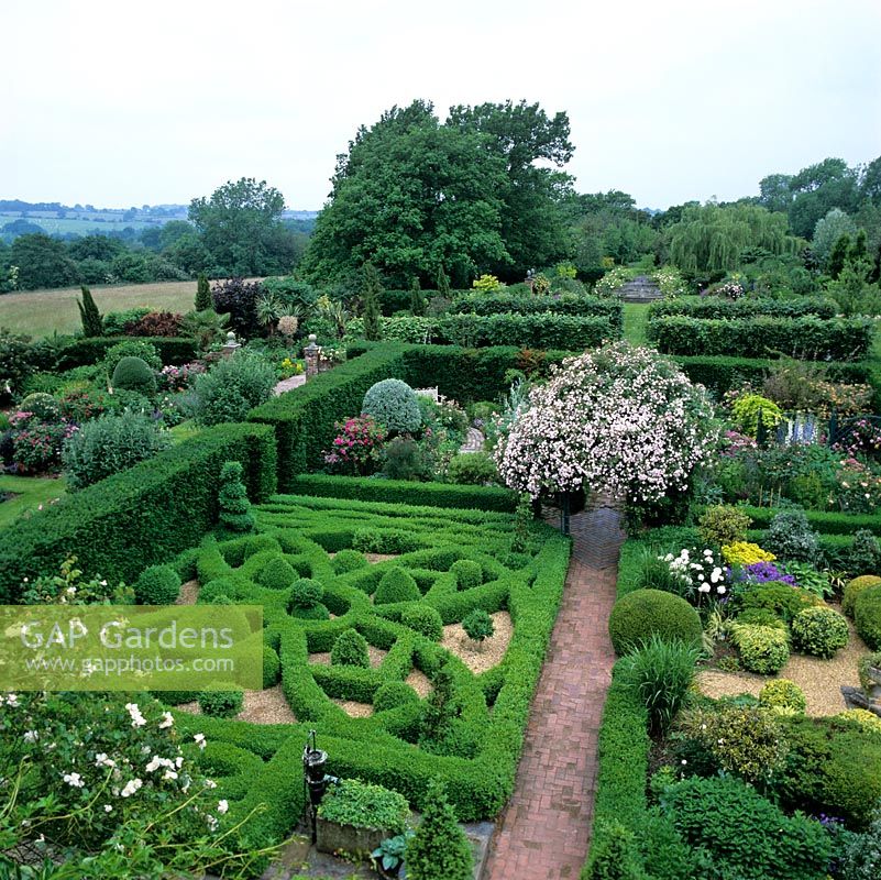 First floor view of Rose Arbour, Gertrude Jekyll, Silver Pear, Gravel and Knot gardens separated from herbaceous borders by yew hedge. Rural landscape beyond.
