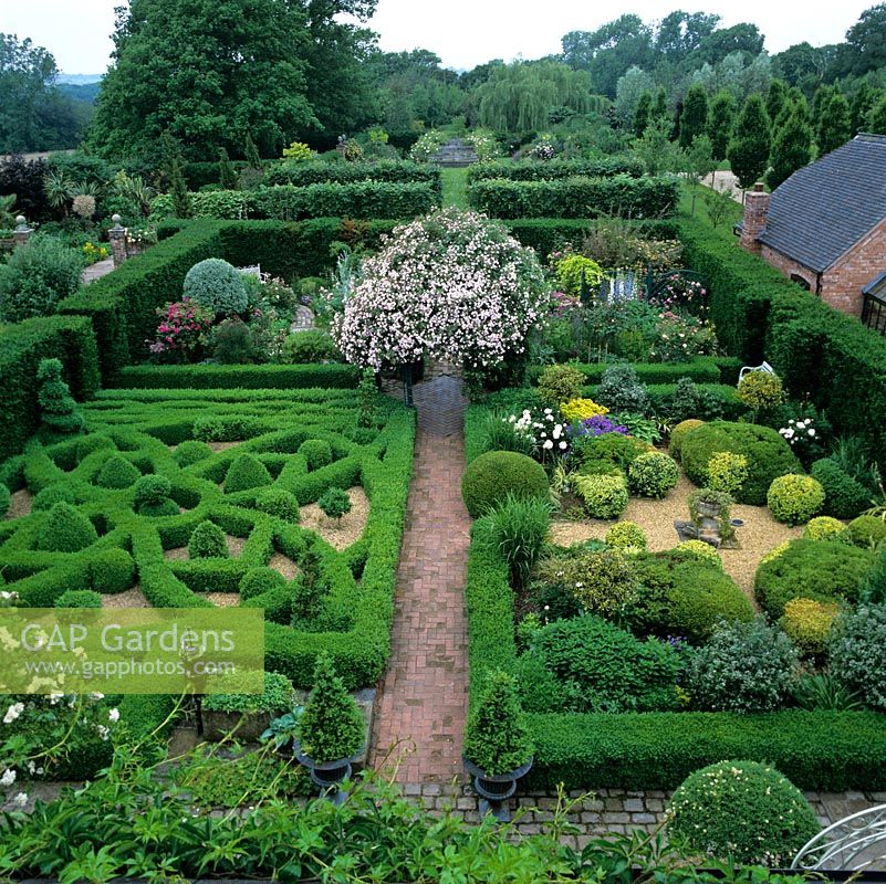 First floor view of Rose Arbour in centre of Gertrude Jekyll, Silver Pear, Gravel and Knot gardens. Pleached lime alley and Fountain Garden beyond. Rural, wooded landscape.