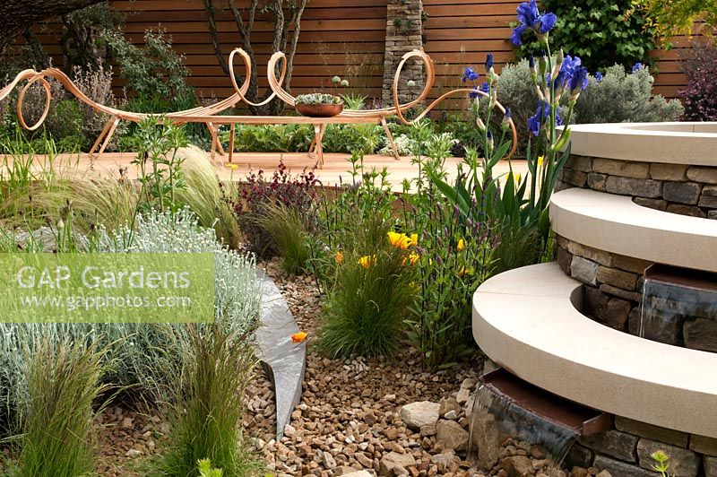 Royal Bank of Canada Garden. Garden seat created out of steamed bent wood by Tom Raffield with Iris mer du sud and Eschscholzia californica growing in the gravel by the water pools