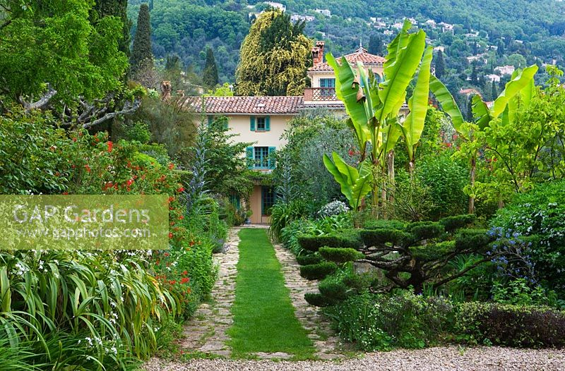 Grass pathway leads to villa through wide flower borders of front garden