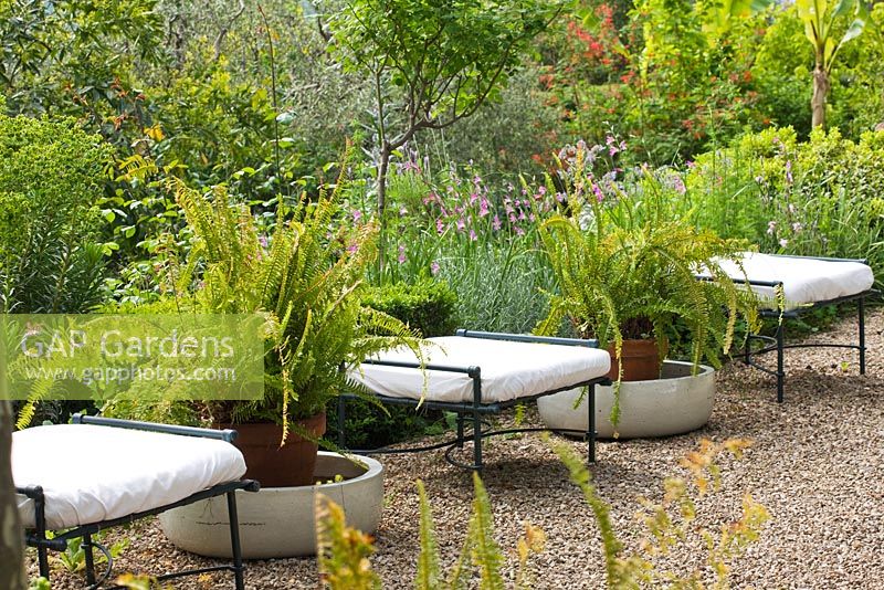 Row of cushioned stools on gravel terrace in french garden, with ferns in pots