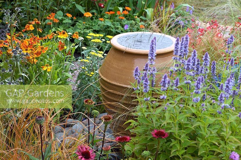 Terracotta pot water feature in colourful flowerbed