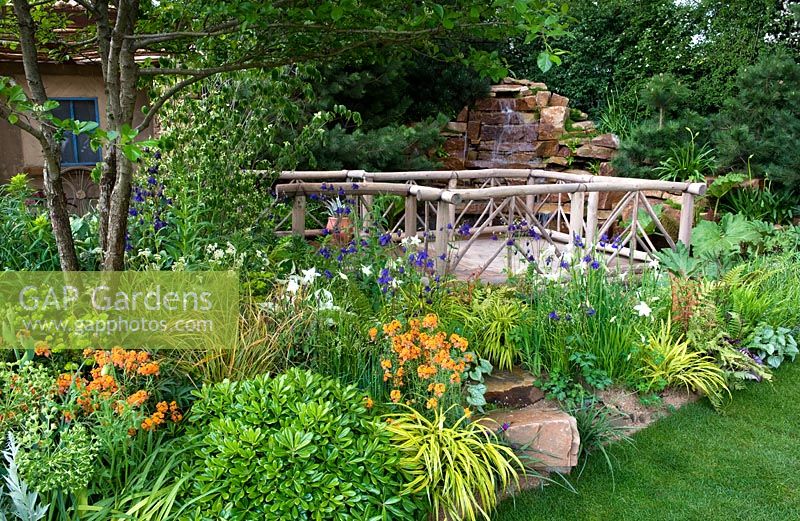 Deck overlooking water feature cascade surrounded by planting. Sentebale - Hope in Vulnerability garden. RHS Chelsea Flower Show, 2015
