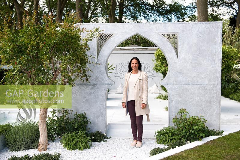 The Beauty of Islam, portrait of the garden designer Kamelia Bin Zaal against the wall with Arabic words, poem surrounded by Punica granatum and Cistus salviifolius. RHS Chelsea Flower Show, 2015