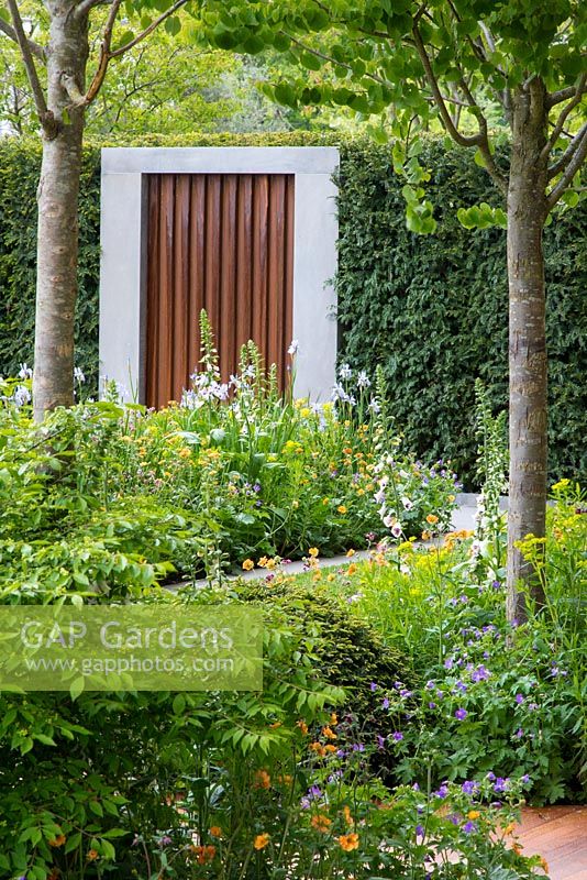The Homebase Garden - Urban Retreat. Corten steel and concrete door. Planting includes Geum 'Totally Tangerine', Geum rivale, Digitalis 'Pam's Choice' and geraniums.
