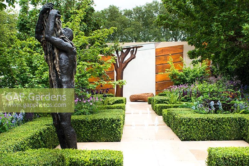 The Morgan Stanley Healthy Cities Garden. View of bronze sculpture and stone path with water feature leading to the wall covered with steel panels. Symmetric hedges of buxus sempervirens, fern - Dryopteris affinis, Salvia nemorosa 'Caradonna', Camassia cusickii and Lupinus 'Masterpiece'. 