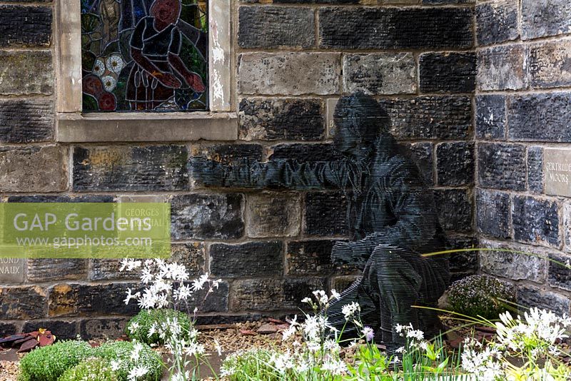 Side view of ethereal and transforming steel sculpture of young RAF pilot by John Everiss. Lychnis flos-cuculi - White ragged robin in foreground. Evaders Garden. RHS Chelsea Flower Show, 2015