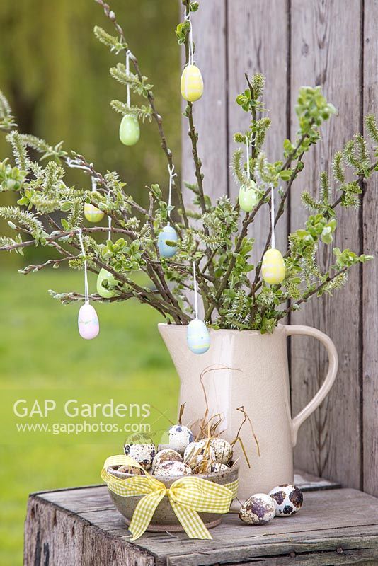 Decorative eggs hanging from fresh spring foliage, accompanied with a bowl of Quail eggs and a view to the garden