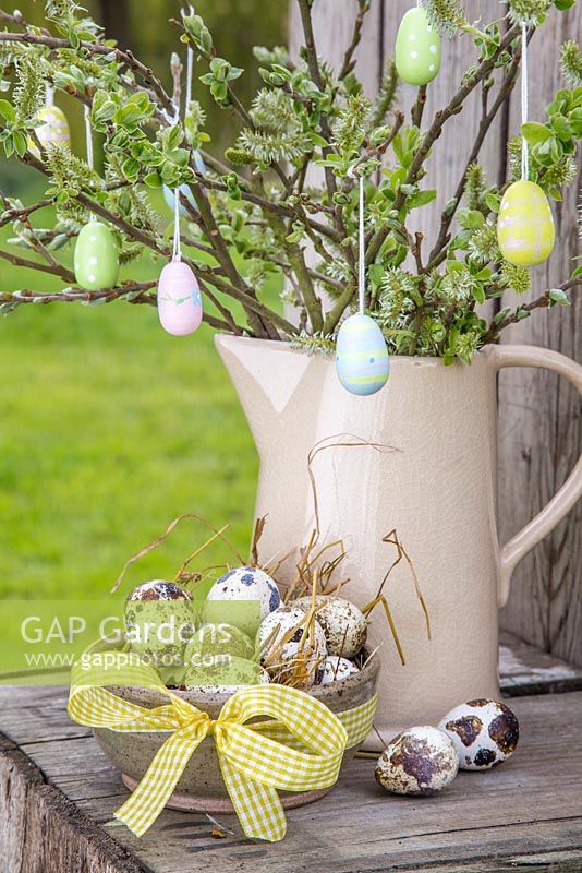 Decorative eggs hanging from fresh spring foliage, accompanied with a bowl of Quail eggs and a view to the garden