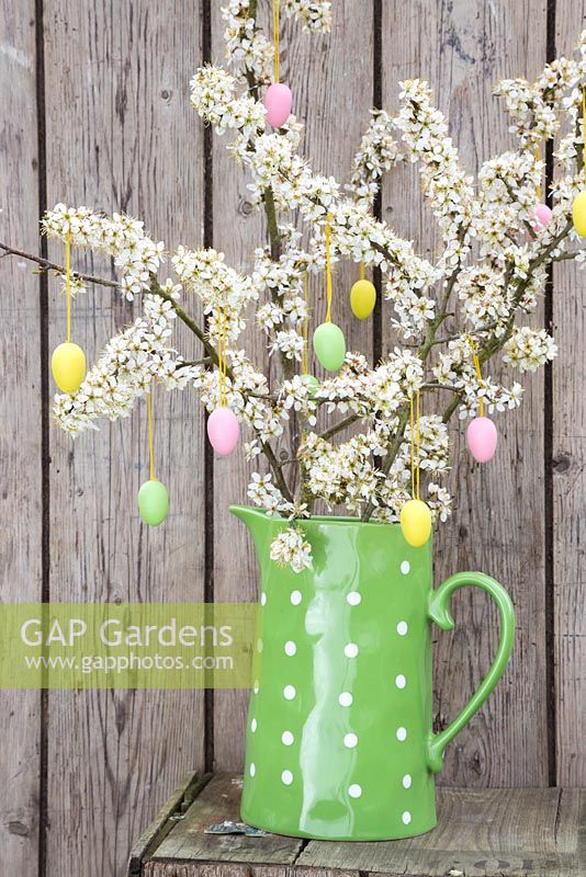 Decorative eggs hanging from blossoming spring foliage, in a green polkadot jug