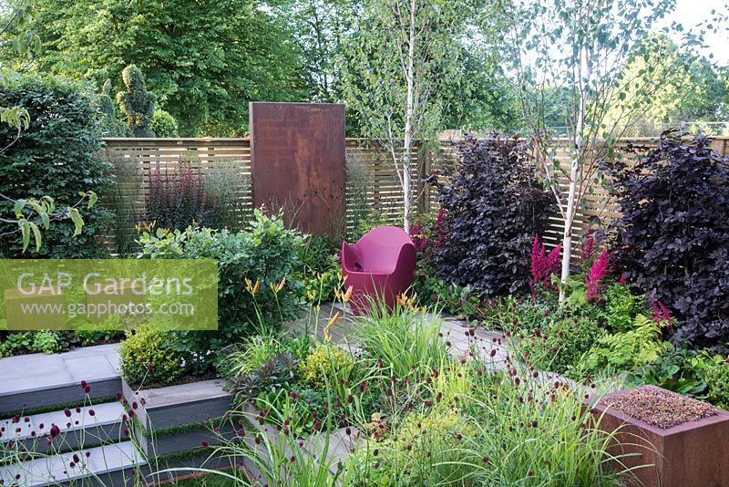 Foundation for Growth Garden with O-nest chair by Tord Boontje, slatted fencing with Fagus sylvatica 'Atropurpurea', Betula utilis var. jacquemontii and Astilbe x ardensii 'Fanal', Sanguisorba officinalis 'Morning Select' in foreground, RHS Hampton Court Palace Flower Show 2015