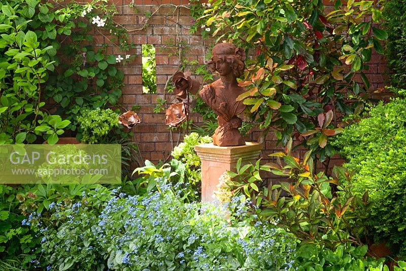 Rusty lady sculpture with Brunnera macrophylla 'Jack Frost' - Siberian bugloss 'Jack Frost'. The Court, North Ferriby, Yorkshire, UK. Spring, May 2015.