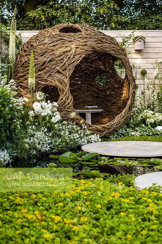 Living Landscapes 'City Twitchers' - view across pond and circular paved areas towards spherical willow bird hide and nesting box with mixed white planting - RHS Hampton Court Flower Show 2015