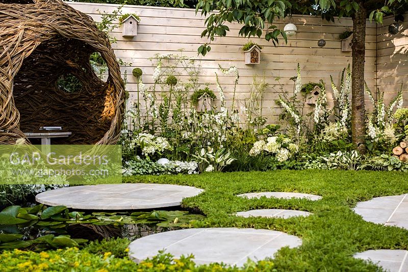 Living Landscapes 'City Twitchers' - view showing circular paved areas, camomile lawn, pond, spherical willow bird hide, nesting boxes, prunus tree and mixed white planting - RHS Hampton Court Flower Show 2015