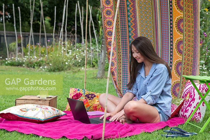 Young girl using a laptop in a sun canopy created with fabric and minimal materials