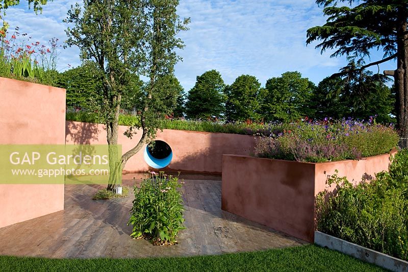 Pink painted raised bed with slope planted with perennials surrounding cork oak surface in contemplative space. SABO - The Circle of Life, Sponsor - Sabo Oil.  Silver-gilt medal, RHS Hampton Court Palace Flower Show 2015