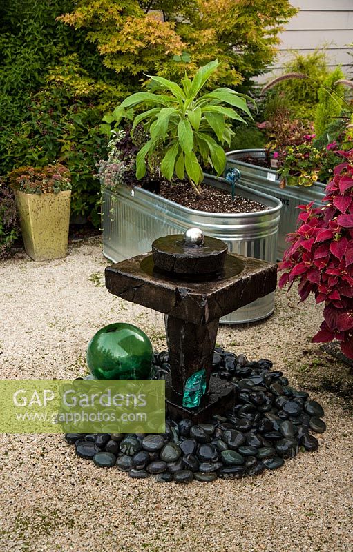 Water feature with decorative stones and glass ball.  Raised beds made from galvanized metal baths.  Mixed planting with Echium, Cistus, Hypericum, Acer 