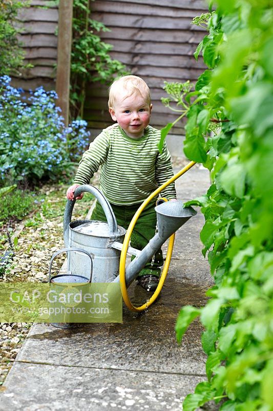 Little boy playing with watering cans and hose pipe