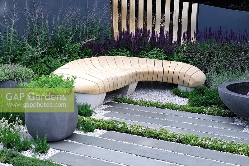 Urban garden with carved, bleached oak bench and grey stone pots on polished stone patio - Living Landscape: Healing Urban garden - RHS Hampton Court Palace Flower Show 2015
