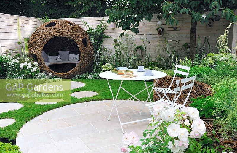 Circular seating area surrounded by a chamomile lawn, with bistro table and chairs and woven willow bird hide with extensive planting to attract insects and birds - Living Landscapes 'City Twitchers', RHS Hampton Court Flower Show 2015