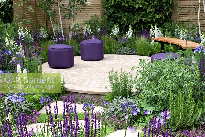 Purple feminine planting with circular paving in seating area, and stepping stones marking the decaces since the Charity's inception in The Wellbeing of Women Garden at RHS Hampton Court Palace Flower Show 2015