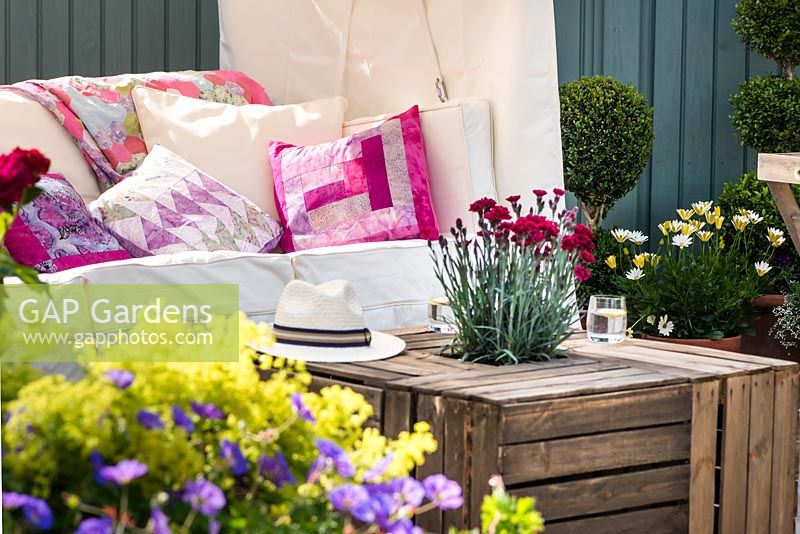 Just Retirement: A Garden For Every Retiree, view of seating area with table made from wooden crates with Dianthus and summer flowers. Designer: Tracy Foster Sponsor: Just Retirement Ltd