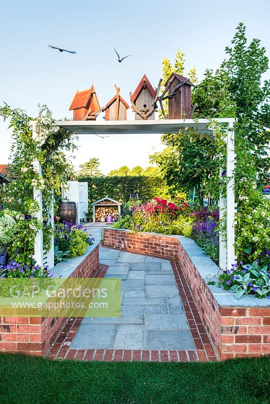 Just Retirement: A Garden For Every Retiree, view of white pergola with birdhouses and birds at the entrance to rural garden. Designer: Tracy Foster Sponsor: Just Retirement Ltd