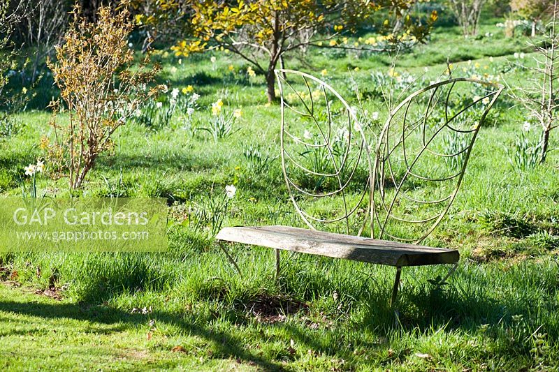 Decorative bench with back rest formed of metalwork leaves sited within the oak circle. Moors Meadow Garden and Nursery, Bromyard, Herefordshire, UK