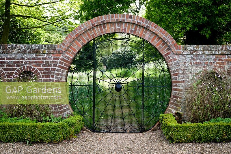Hoveton Hall: The Spider Gate, looking from walled garden to woodland. Gravel pathway with box - Buxus sempervirens edging and Felicia petiolata in arches