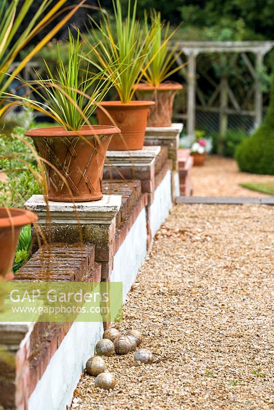 Terracotta pots containing cordylines on the side of a raised boules allee