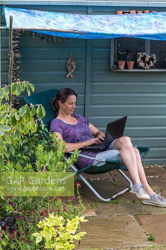 Woman sitting under a blue awning, using a laptop computer 