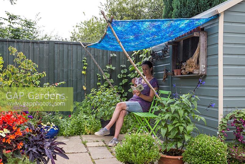 Woman reading a book and drinking tea under a blue shaded awning