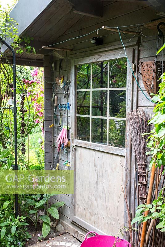 Garden shed entrance with trellis as a holder for gloves and other garden tools, next to the door, a broom, Digitalis purpurea