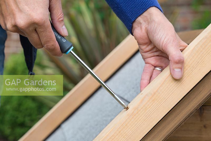 Using a screwdriver  to attach the wooden batons to the outer rim of the kennel roof
