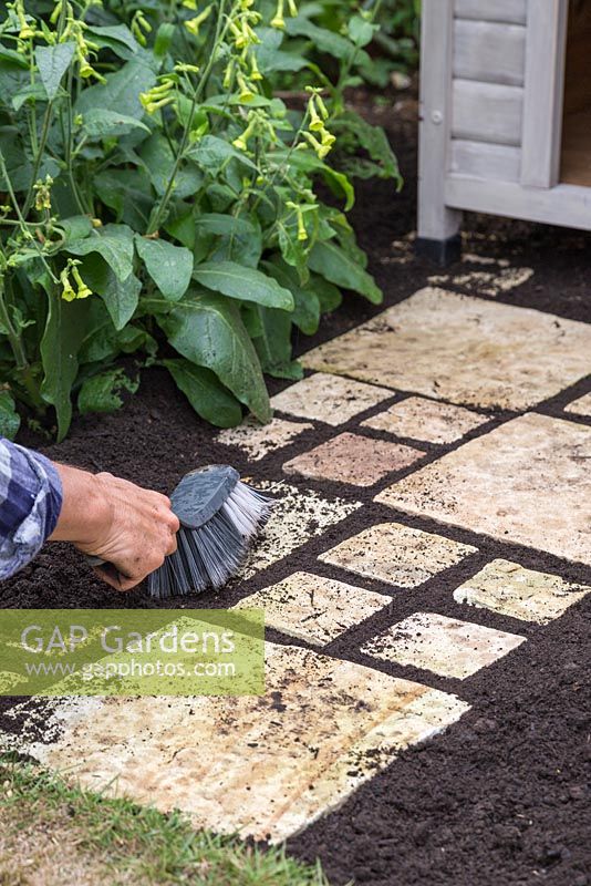 Using a hand brush to fill the gaps in the path with soil