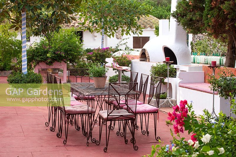 Patio with red floor, metal table and chairs, outdoor kitchen with barbeque and pizza oven.  Alaior, Menorca. 