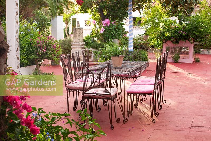 Patio with red floor, metal table and chairs bouginvillea, painted tree trunk - blue and white stripes. Alaior, Menorca.