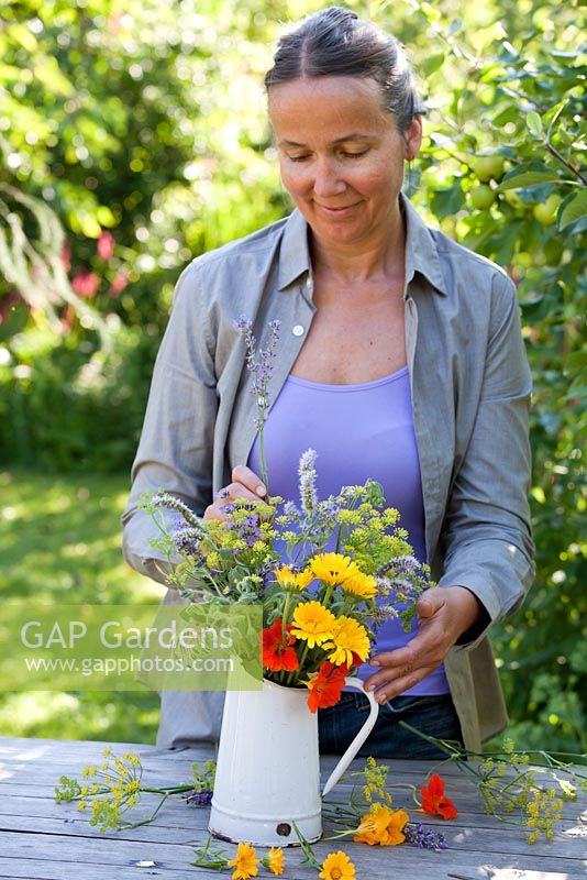Woman making an arrangement - Jug of herb and edible flowers - marigold, fennel, borago, mint, nasturtium