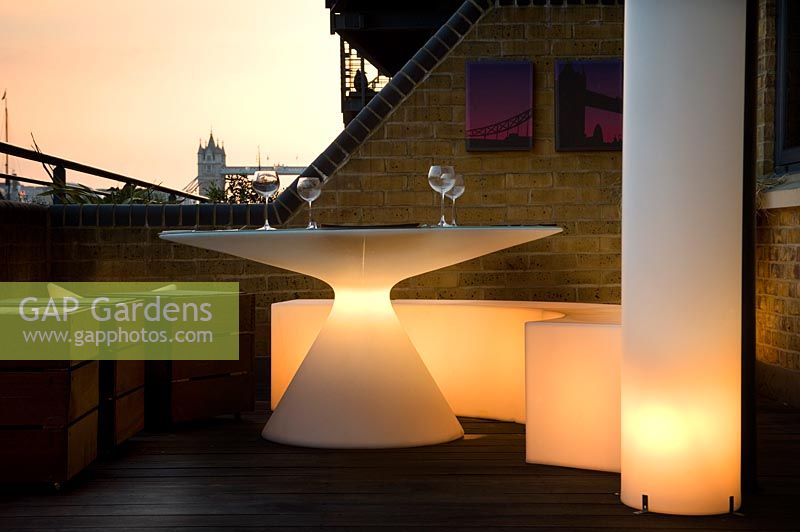 Contemporary balcony overlooking the Thames at Wapping with illuminated white plastic dining furniture in small space 