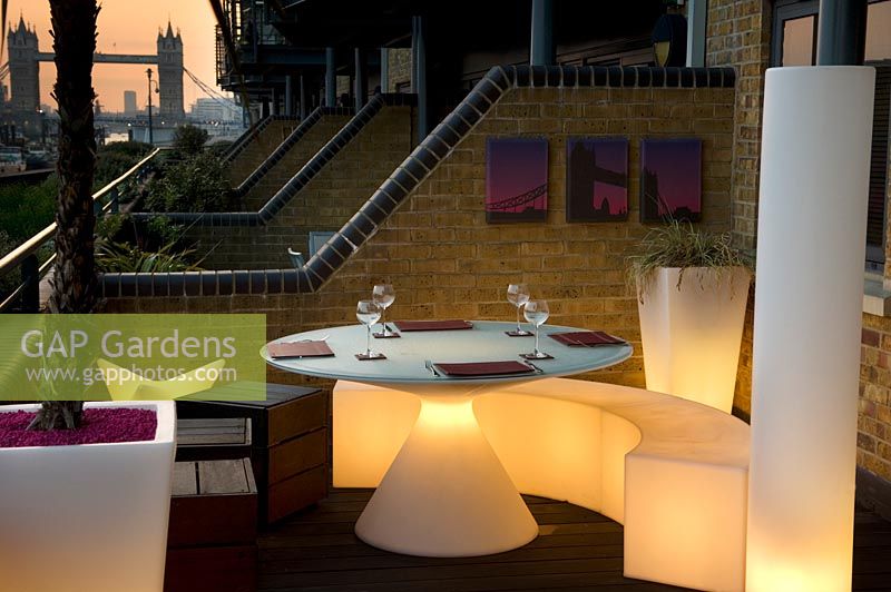Contemporary balcony overlooking the Thames at Wapping with lit white plastic dining furniture in small space.  Wapping Balcony