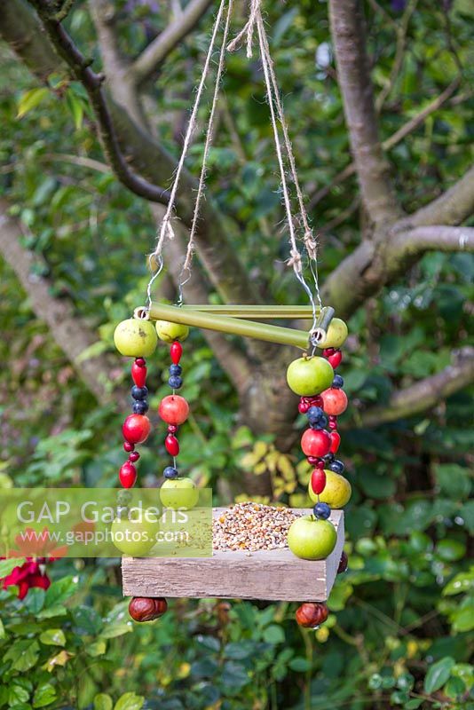 A Berry House bird feeder constructed from Bamboo, Wood, Conkers, Wire, String, Crab Apples, Sloe berries, Rose hips and Hawthorn berries