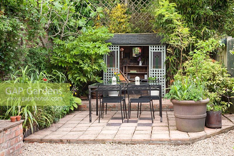Summer house and eating area in the Secret garden with Fatsia japonica, a Fig tree, Hosta and Melianthus major. Hope House, Caistor, Lincolnshire, UK.