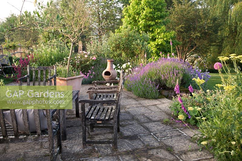 Garden patio furniture and chiminea in summer country garden with Lavender, Digitalis, Rosa Geranium and Penstemon. Bradness Gallery, East Sussex. Owners: Artists Michael Cruickshank and Emma Burnett