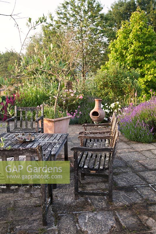 Garden patio furniture and chiminea in summer country garden with Lavender, Digitalis, Rosa, Geranium and Penstemon. Bradness Gallery, East Sussex. Owners: Artists Michael Cruickshank and Emma Burnett