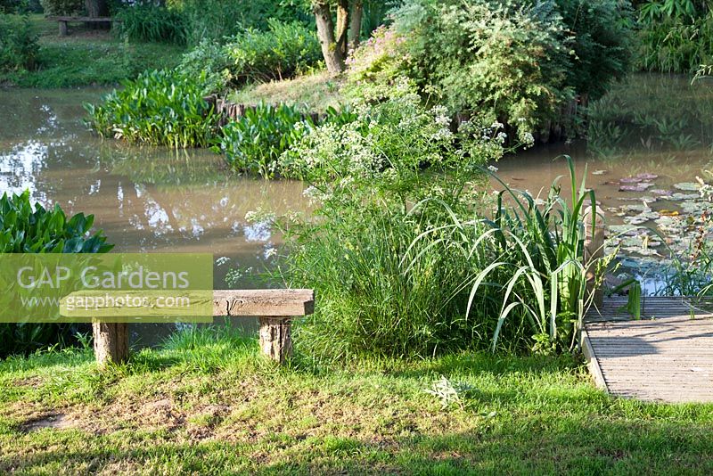 Rustic wooden bench overlooking landscaped lake in country garden with jetty. Bradness Gallery, East Sussex. Owners: Artists Michael Cruickshank and Emma Burnett