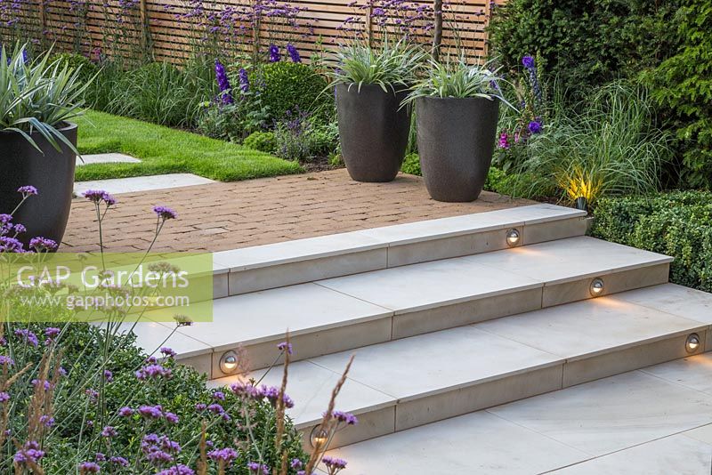 Marble steps with lighting feature at dusk. Verbena bonariensis and Calamagrostis x acutiflora 'Karl Foerster' in foreground and potted Astelia chathamica