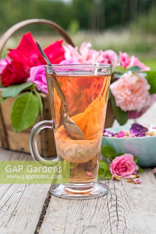 A glass of rose tea with a trug of cut roses and petals