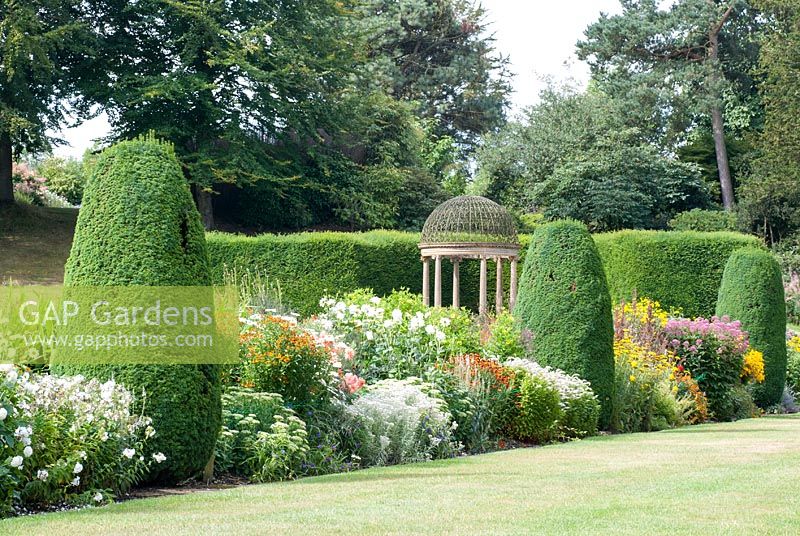 The long border at Forde Abbey, Somerset with clipped Yew pillars and Ionic Temple behind