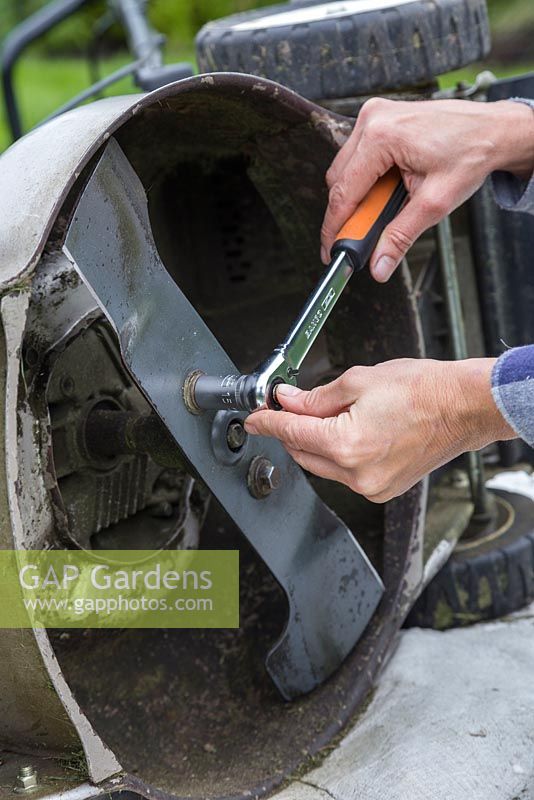 Reattaching the reconditioned and sharpened lawn mower blade with a socket and spanner set